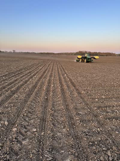 Tractor working dark spring soil under a pink dusk sky